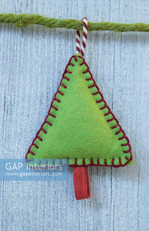 Making stitched felt christmas decorations - miniature christmas tree made from felt and decorative string, hanging against a wooden panel