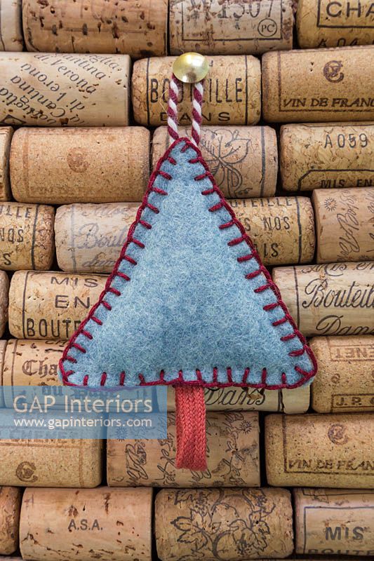 Making stitched felt christmas decorations - miniature christmas tree made from felt and decorative string, hanging against a wine cork board