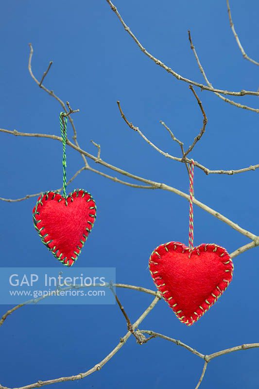 Red hearts stitched together with felt fabric, hanging from  twigs