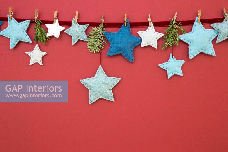 A variety of coloured felt stars hanging against a red background 