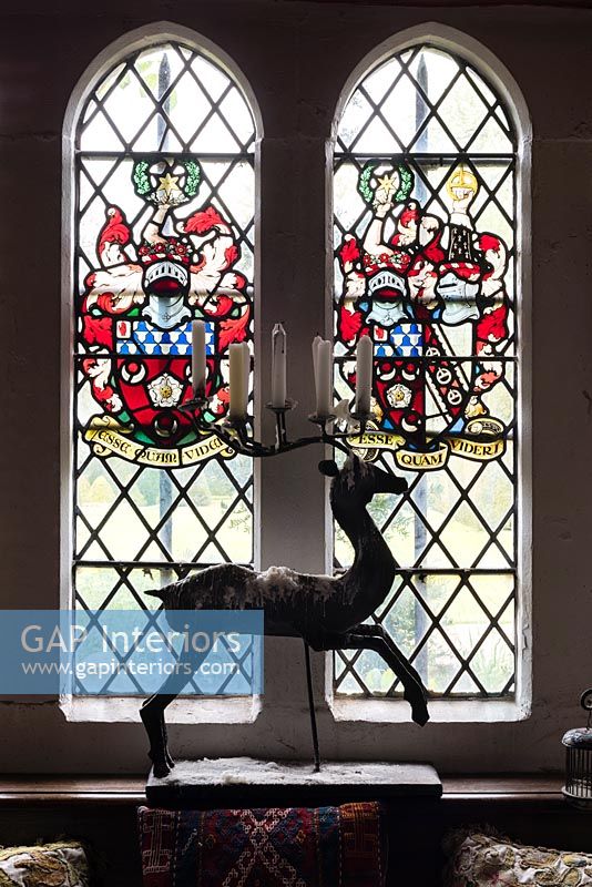Decorative metal candlestick in the form of a leaping hart in front of the stained glass window which bears the coat of Arms of Sir Francis Cook - Cothay Manor