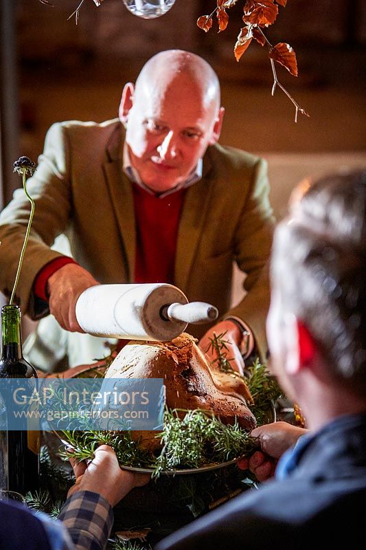 Man serving salt dough wrapped lamb at the decorated dining table 