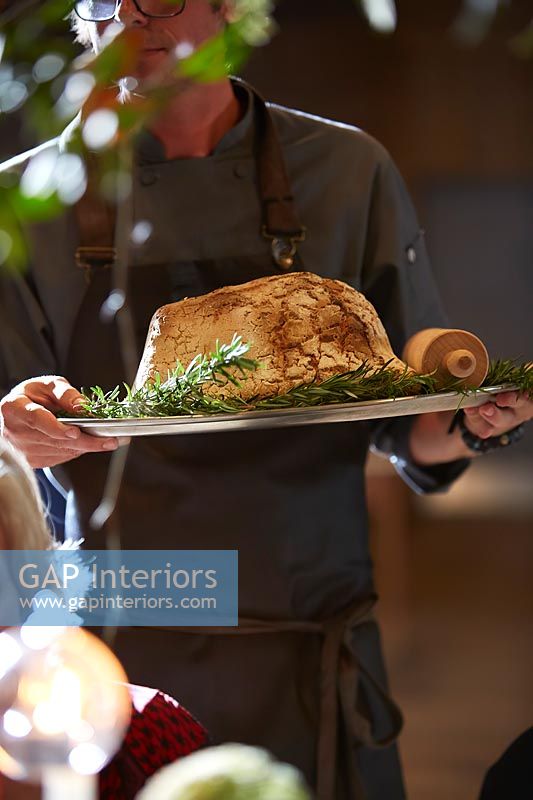 Man carrying tray of slow baked salt dough wrapped shoulder Perthshire lamb with rosemary