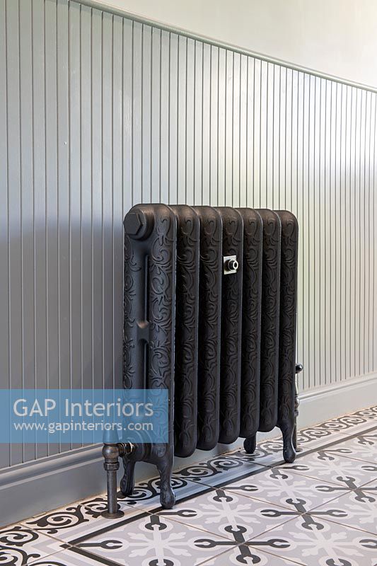 Cast iron radiator against wooden panel and tiled floor