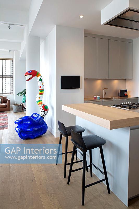 Black kitchen stools and colourful sculpture in modern open plan apartment 