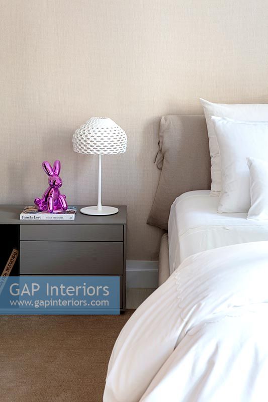 Modern grey bedside table with pink rabbit ornament and white lamp 