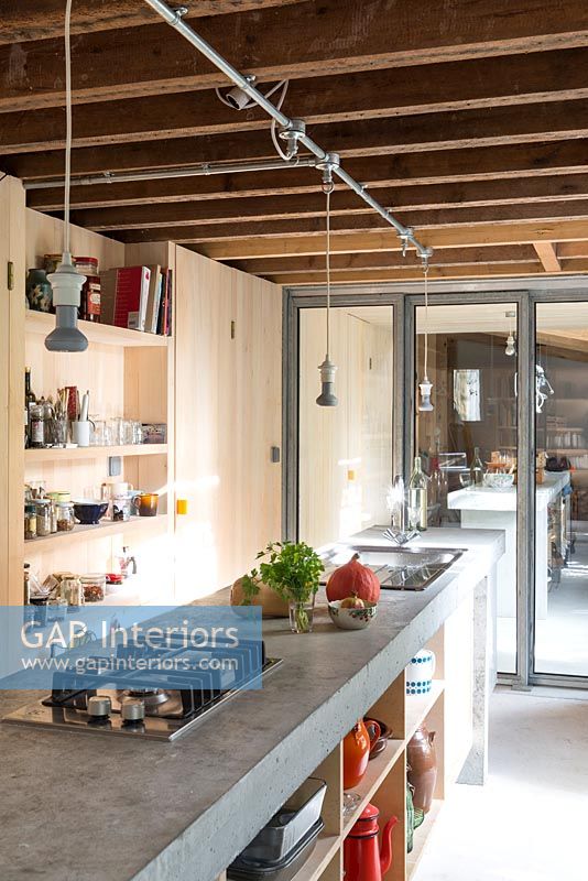 Concrete island and exposed beams in narrow galley kitchen