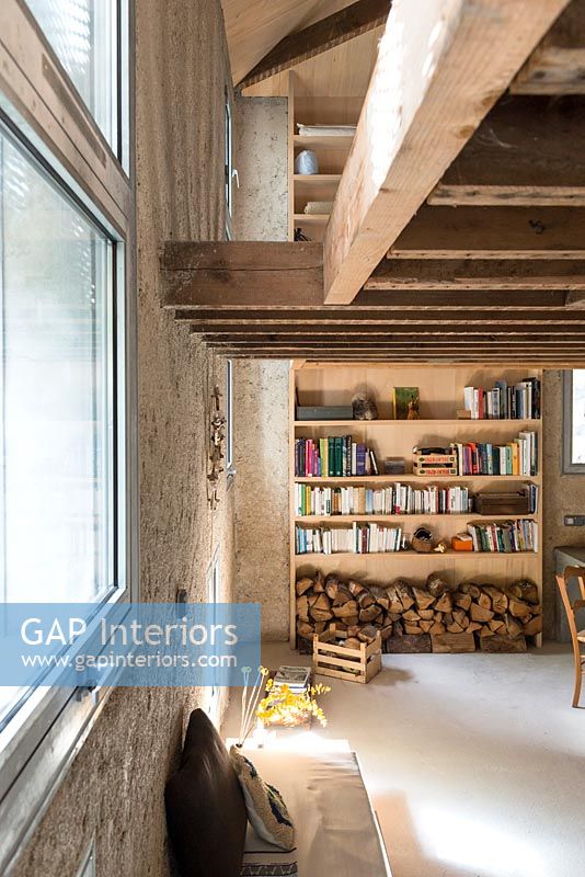 Shelves and log store in narrow living room with exposed wooden beams