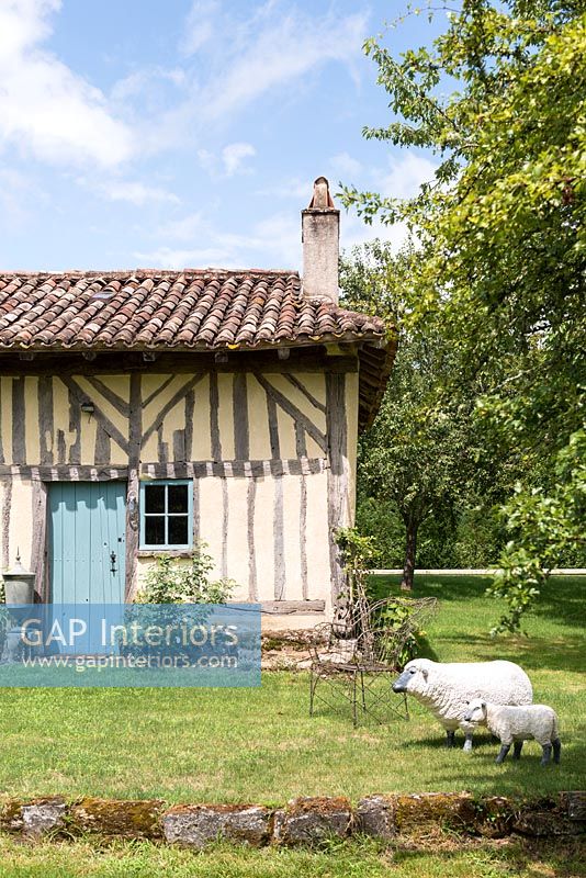 Traditional country house with sheep and lamb sculptures in garden 