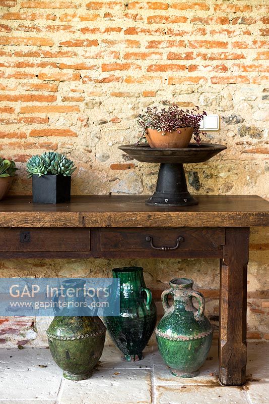 Houseplants on wooden bench by brick wall 