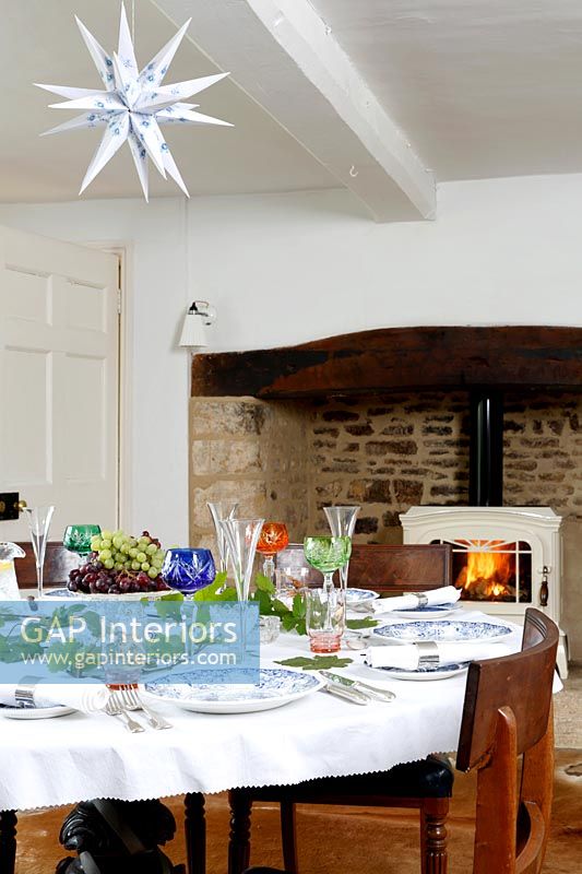 Country dining room with lit log burning stove in large fireplace 