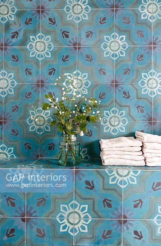 Colourful tiled wall in bathroom  with towels and vase of flowers 
