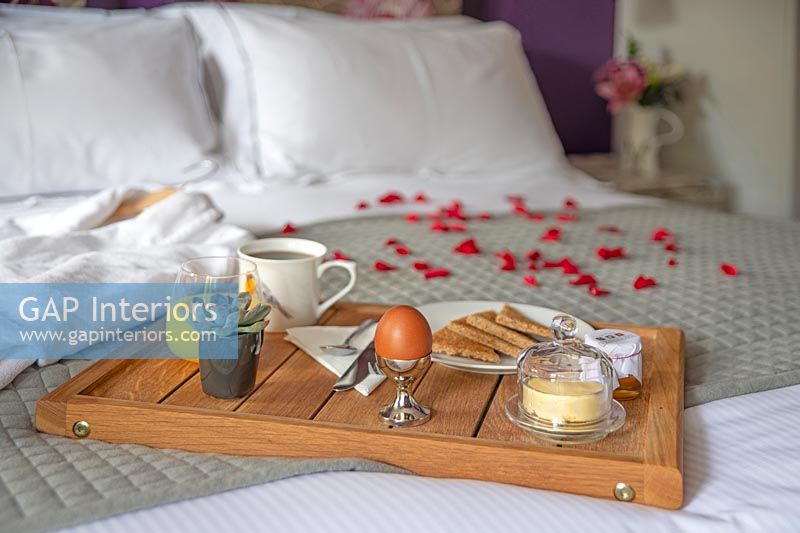 Breakfast tray and bathrobe with rose petals on bed