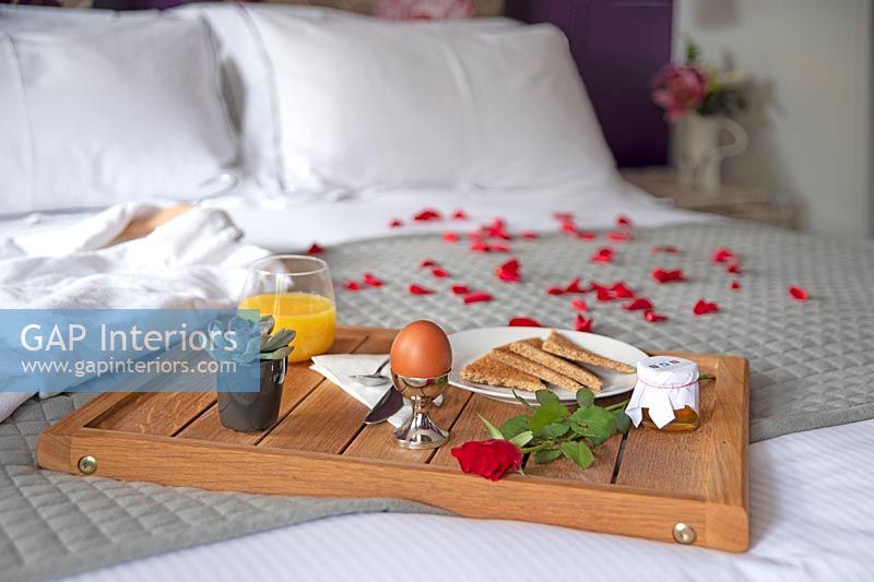 Breakfast tray on bed with rose petals and bathrobe