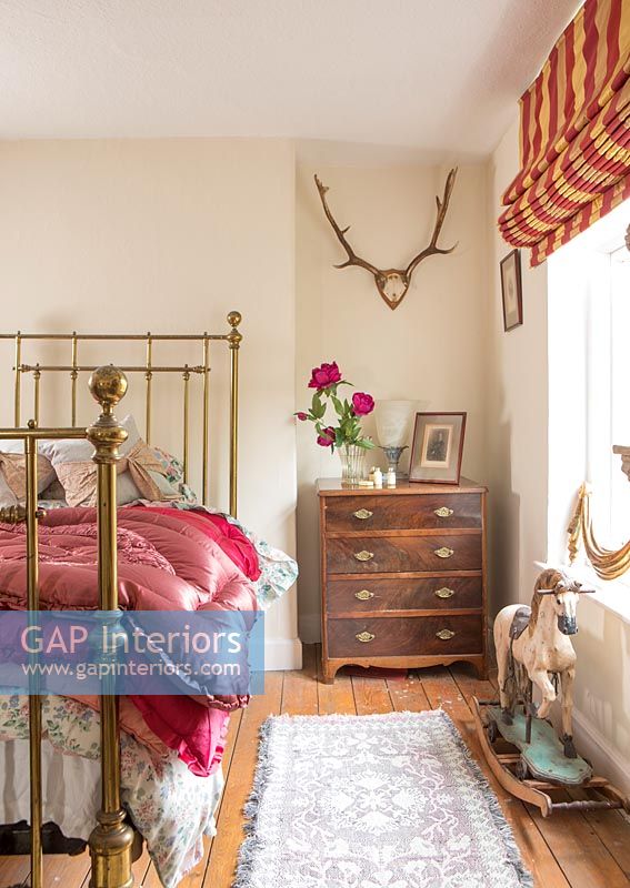 Country bedroom with wall mounted antlers and vintage rocking horse toy 