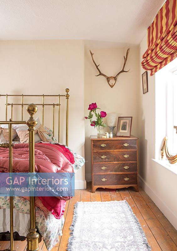 Country bedroom with wall mounted antlers and wooden chest of drawers 