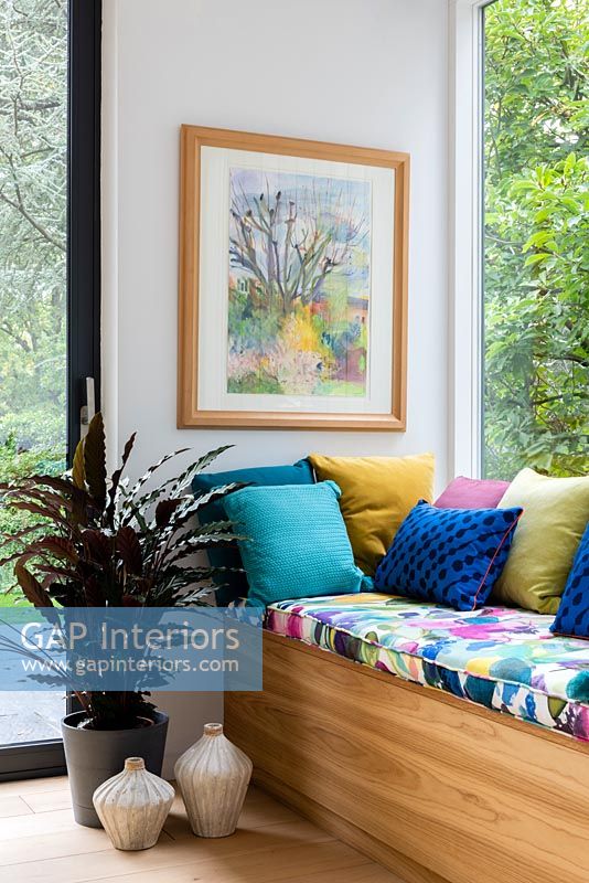 Framed painting above colourful cushions on window seat 