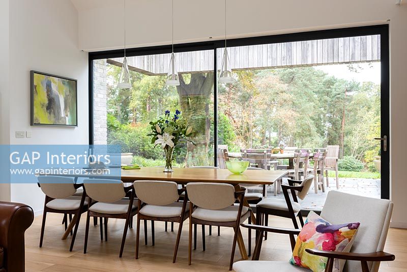 Large dining table by glazed patio doors with views to woodland garden 