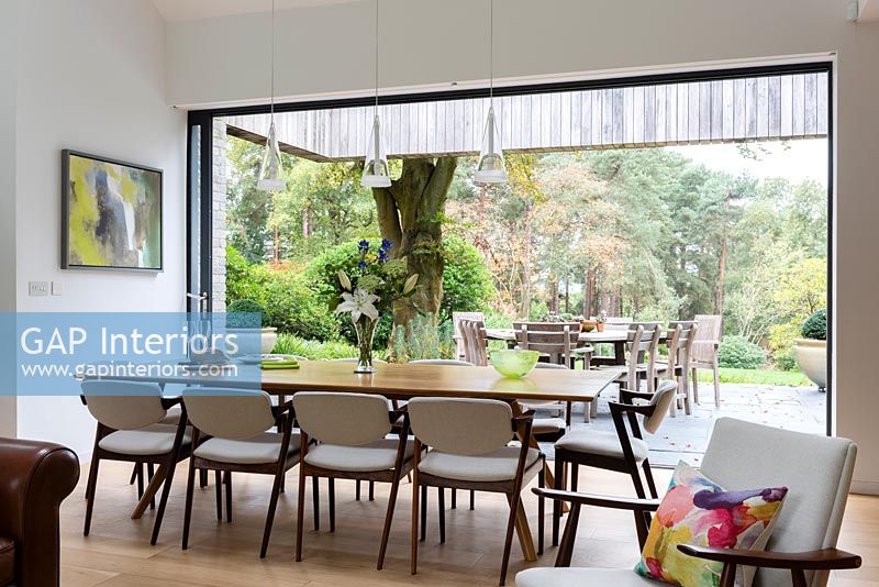 Large dining table by open patio doors with views to woodland gardens 