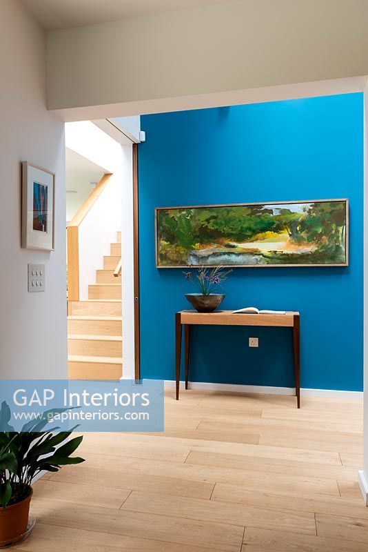 Blue painted feature wall and artwork above console table in modern hallway