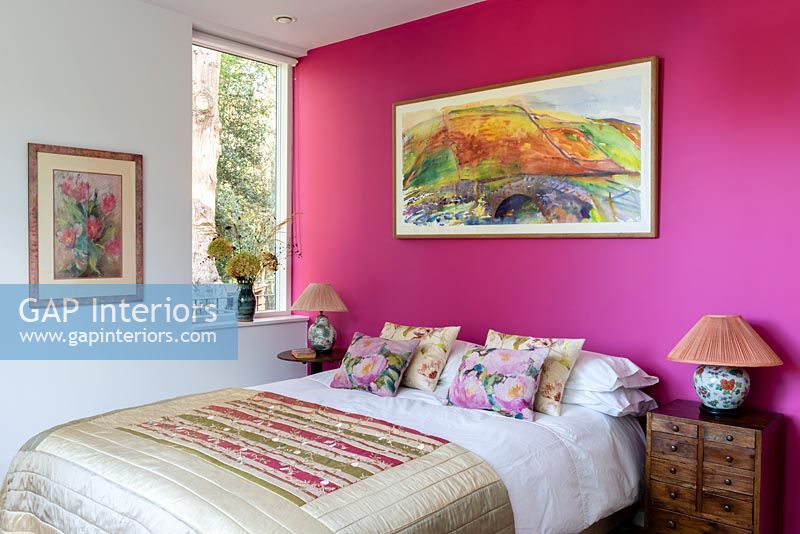 Vivid pink feature wall and colourful artwork in modern bedroom 