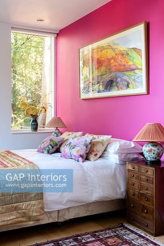 Vivid pink painted wall and artwork in modern bedroom 