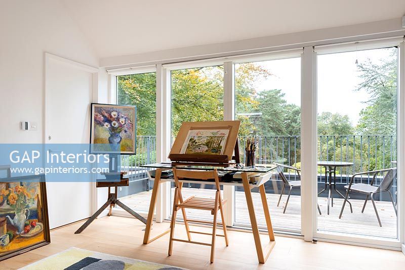 Desk, easel and painting equipment facing windows and balcony 
