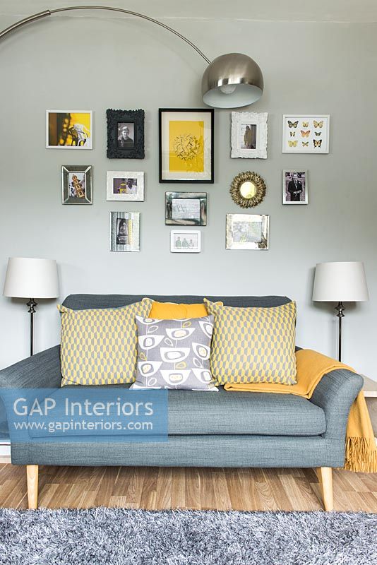 Grey sofa with yellow cushions and display of pictures on grey painted wall 