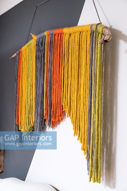 Display of colourful threads hanging on part painted wall