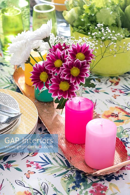 Pink flowers and candles on table with floral tablecloth