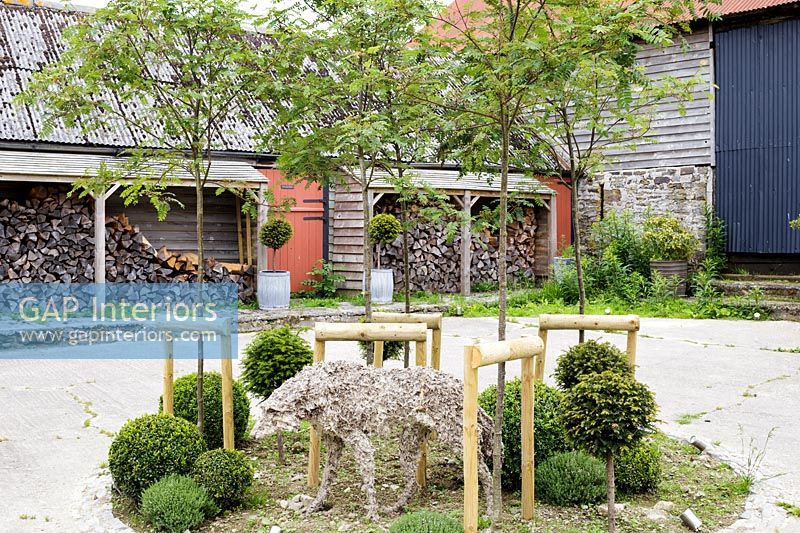 Sculpture of dog in courtyard with log store and outbuildings 