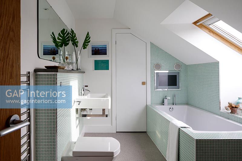 Modern bathroom with mint green tiling and built in television screen 