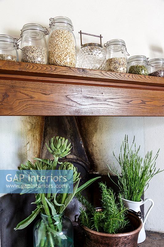 Wooden shelf on chimney breast filled with storage jars and herbs in pots 