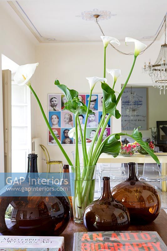 Cut flowers in vase surrounded by coloured glassware