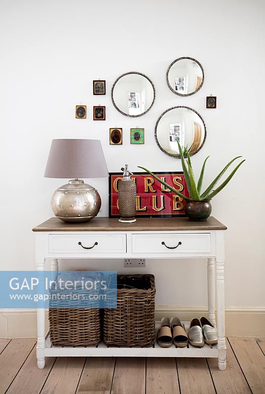 Display of mirrors and small framed pictures above sideboard in hallway 