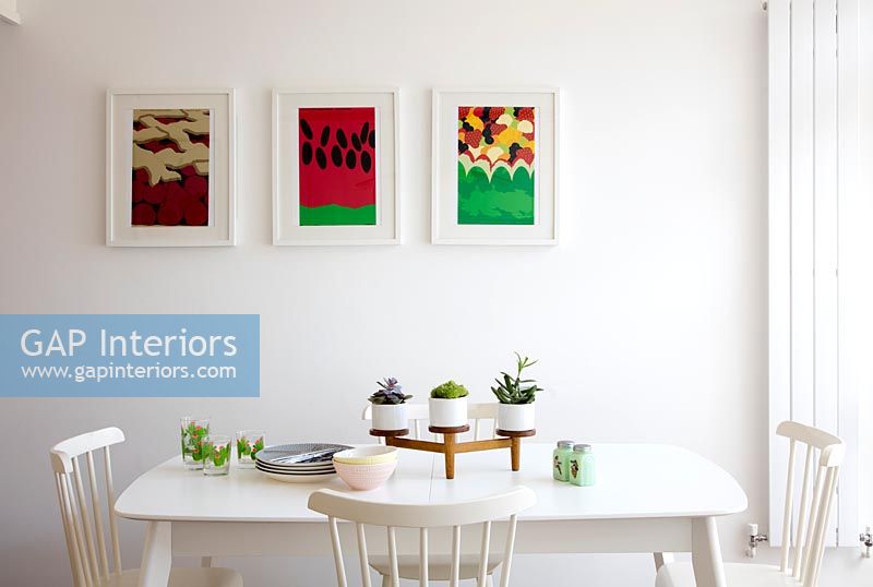 Colourful paintings on wall of white dining room 
