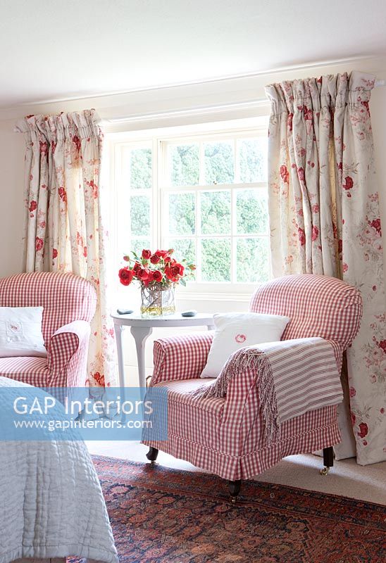 Gingham covered armchairs and floral curtains in country bedroom 