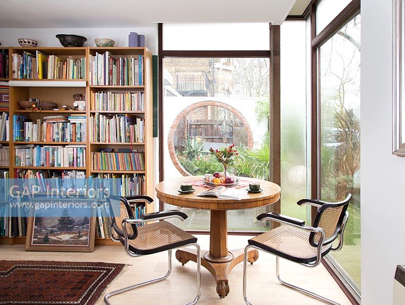 Circular table with chairs in study with bookshelves and large windows 