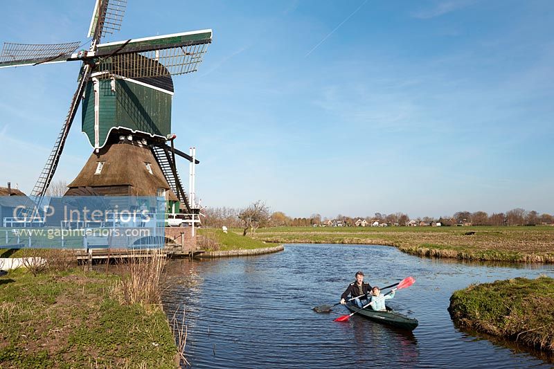 People kayaking alongside windmill  