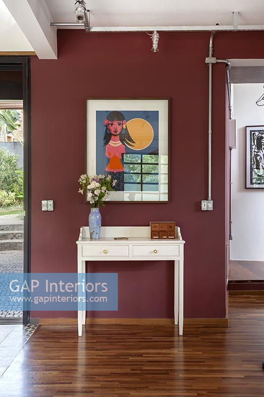 White console table and colourful artwork on dark red painted wall 