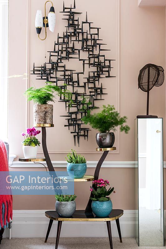 Pink painted wall with black sculpture and vintage plant stand 