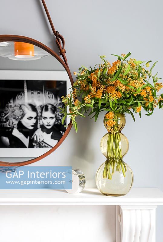 Orange flowers in glass vase on mantelpiece  