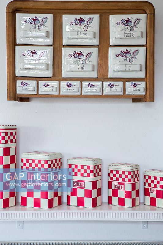 Ceramic storage drawers and set of red and white tins on display 
