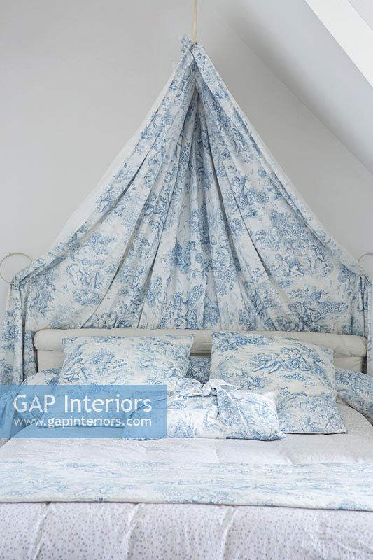 Blue and white fabric canopy over bed with matching cushions 