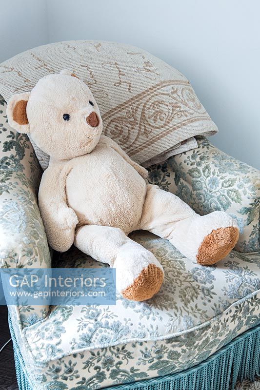 Detail of teddy bear toy on floral armchair 