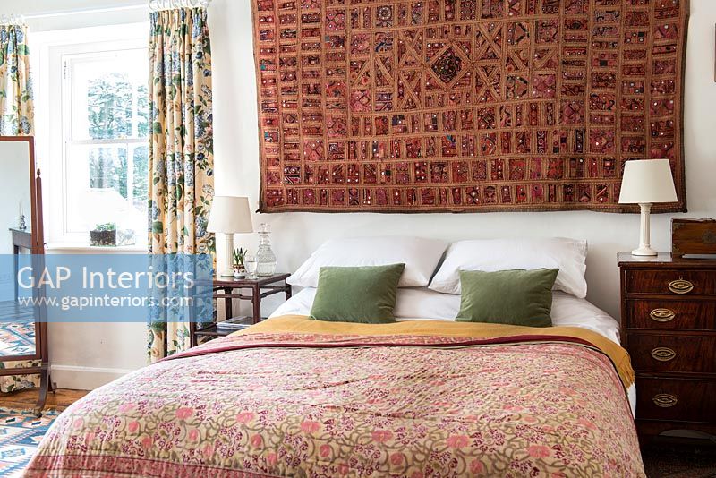 Patterned fabric wall hanging above bed in country bedroom 