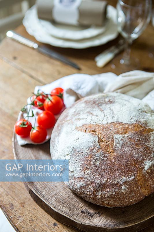 Loaf of uncut bread and tomatoes on rustic dining table 