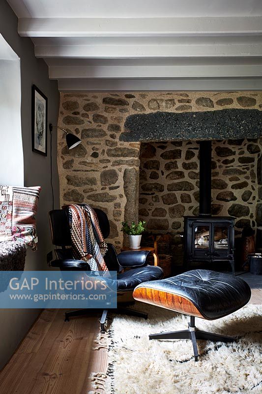Designer chair and footstool next to fireplace in country living room 