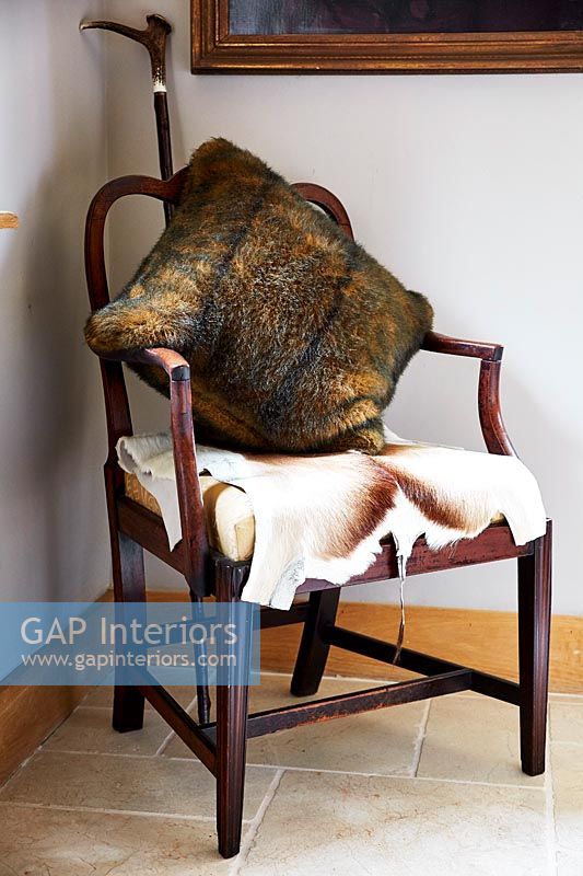 Furry cushion and animal skin on wooden armchair 