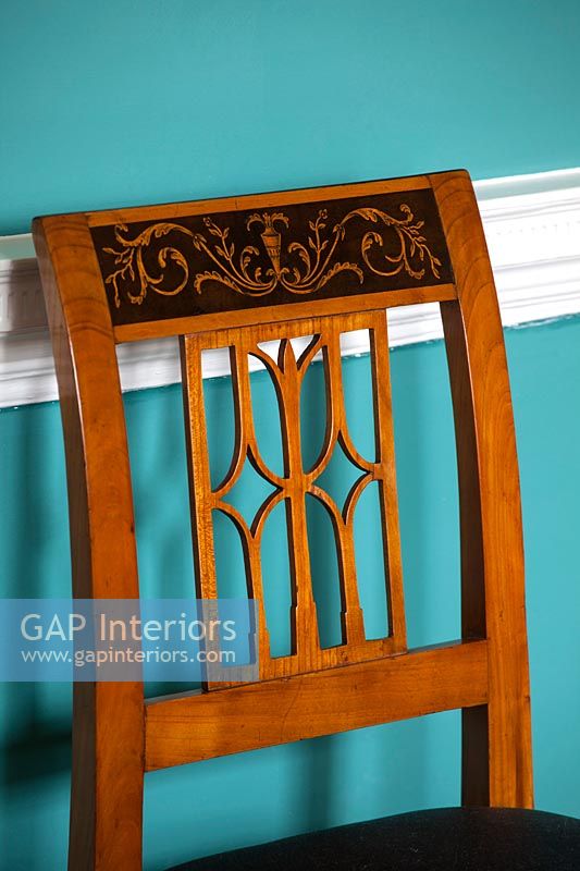 Antique cherry wood dining chair next to dado rail on painted wall 